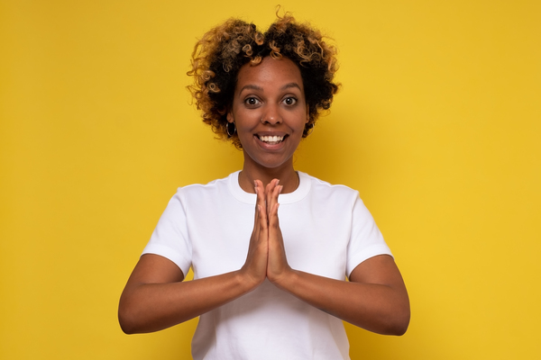 Mulher negra com as mãos juntas e um sorriso em um fundo amarelo representando o sentimento no Setembro Amarelo.